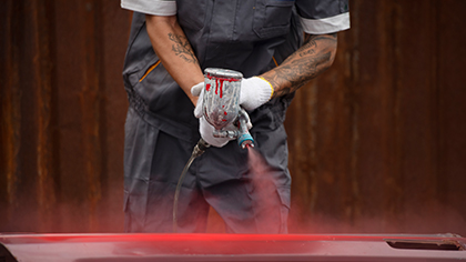 Auto body repair technician using spray gun to apply red paint on vehicle surface, showcasing auto body repair services at Blackstone Complete Auto Care LLC.