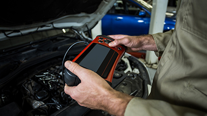 Auto technician using a diagnostic scanner on a vehicle's engine, highlighting auto diagnostics services offered by Blackstone Complete Auto Care LLC.