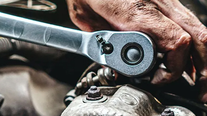 Hand using a ratchet wrench to perform battery and starter repair on a vehicle engine.