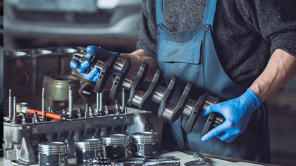 Mechanic assembling engine components, including a crankshaft and pistons, in an auto repair workshop, highlighting engine repair and overhaul services.