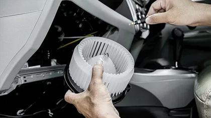 Hands holding a car heater blower motor, demonstrating heating system repair in a vehicle's interior.