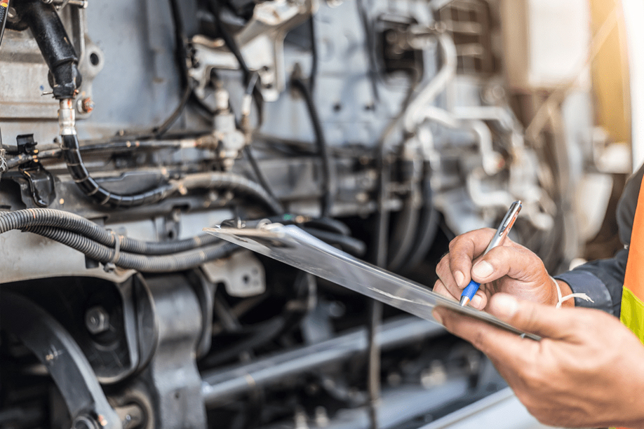 Mechanic inspecting vehicle engine components and taking notes on a clipboard, emphasizing preventive maintenance services in Columbus, OH.