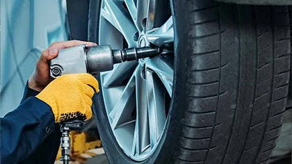 Mechanic using power tool to service vehicle tire, emphasizing tire maintenance and safety in auto repair context.