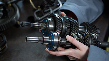 Hands holding a disassembled car transmission gear assembly, showcasing intricate metal components relevant to transmission repair services offered by Blackstone Complete Auto Care LLC.